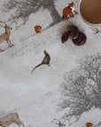 Woodland animal pattern oilcloth with deer, fox, and badger on a textured surface with a cup of coffee.