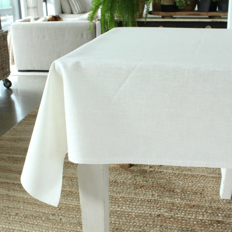 White tablecloth on a table in a room with a couch and plants.
