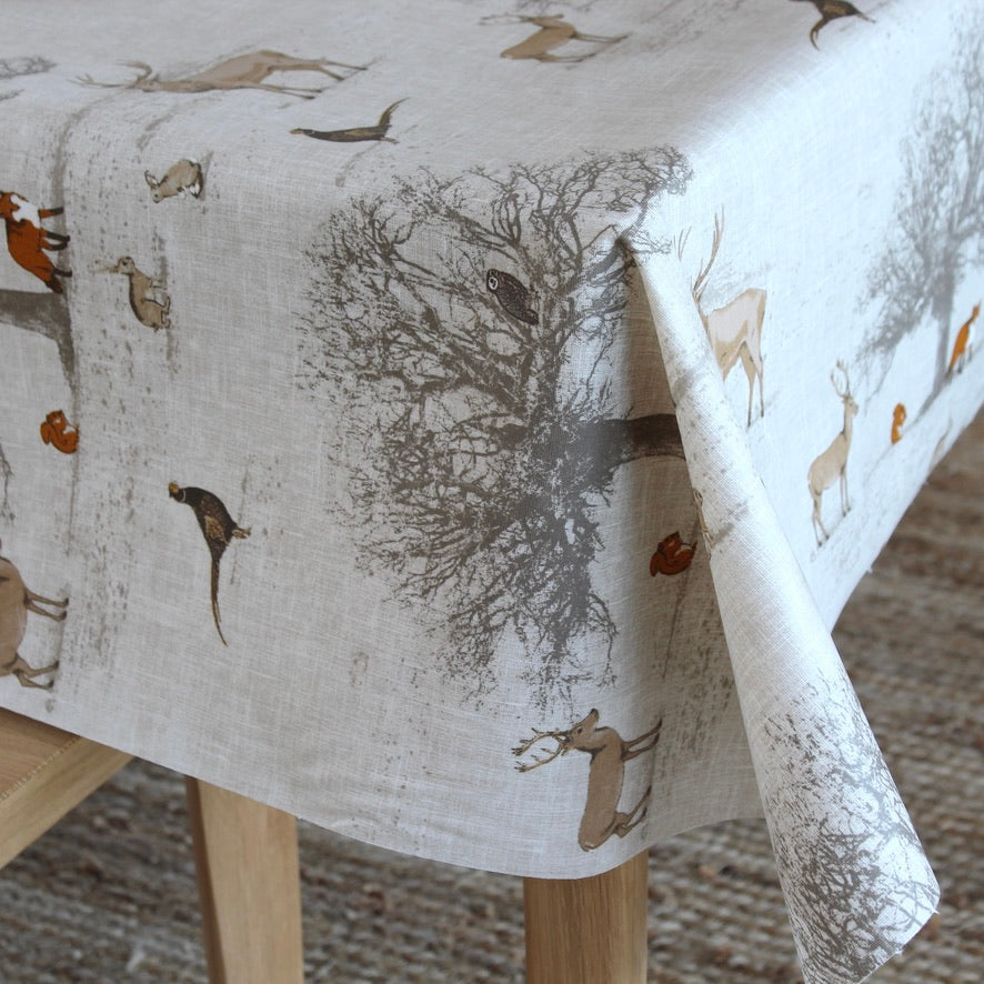Tablecloth with nature-themed design featuring trees and animals on a wooden table.