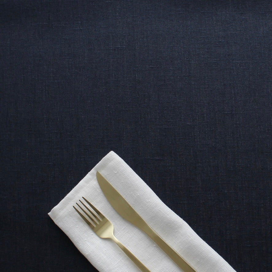Gold fork and knife on a white napkin against a dark blue  tablecloth