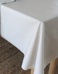 A light beige tablecloth draped over a table with wooden legs, with a striped runner partially visible on the left side over a neutral woven rug.
