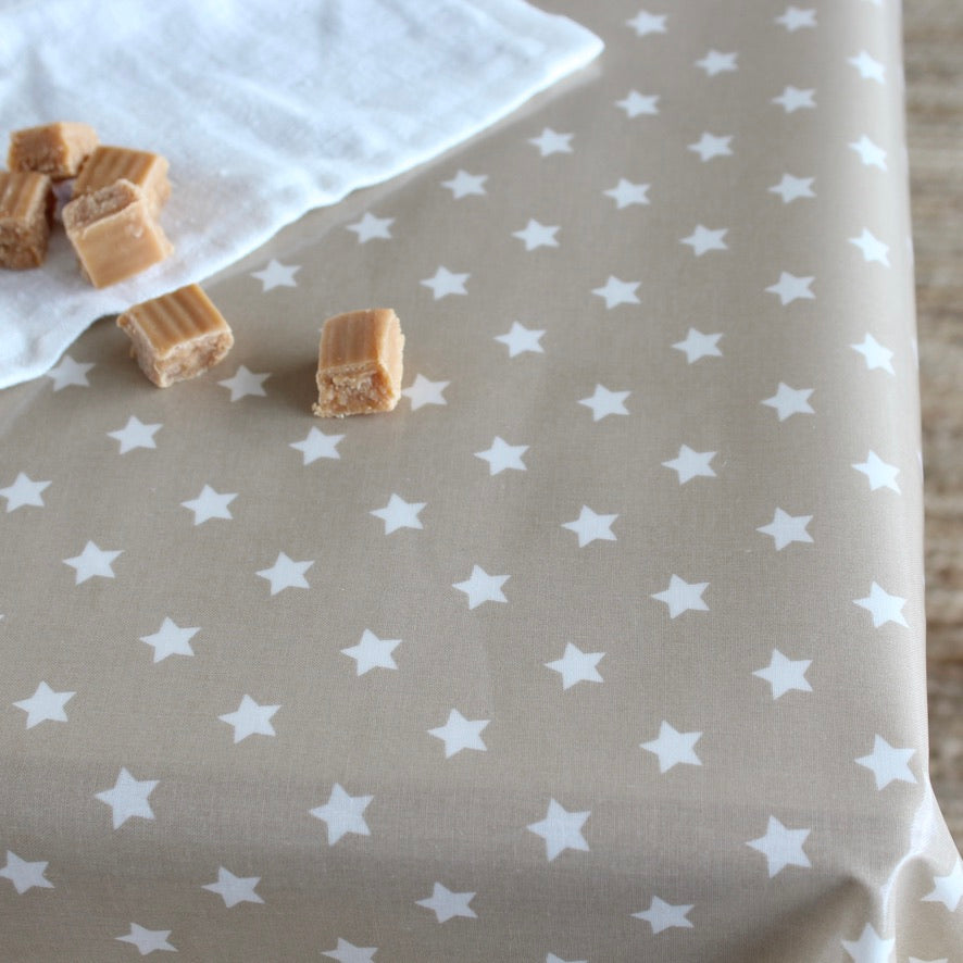 A close-up of a beige oilcloth printed with a repeating pattern of small white stars, with a folded white cloth and a few caramel candy pieces placed on top.