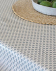 Tablecloth with a geometric pattern on a table, accompanied by a woven placemat and a bowl of green apples.