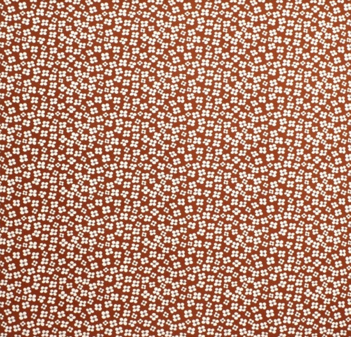 A close-up of a terracotta orange fabric with a dense, small-scale white floral or ditsy print pattern.