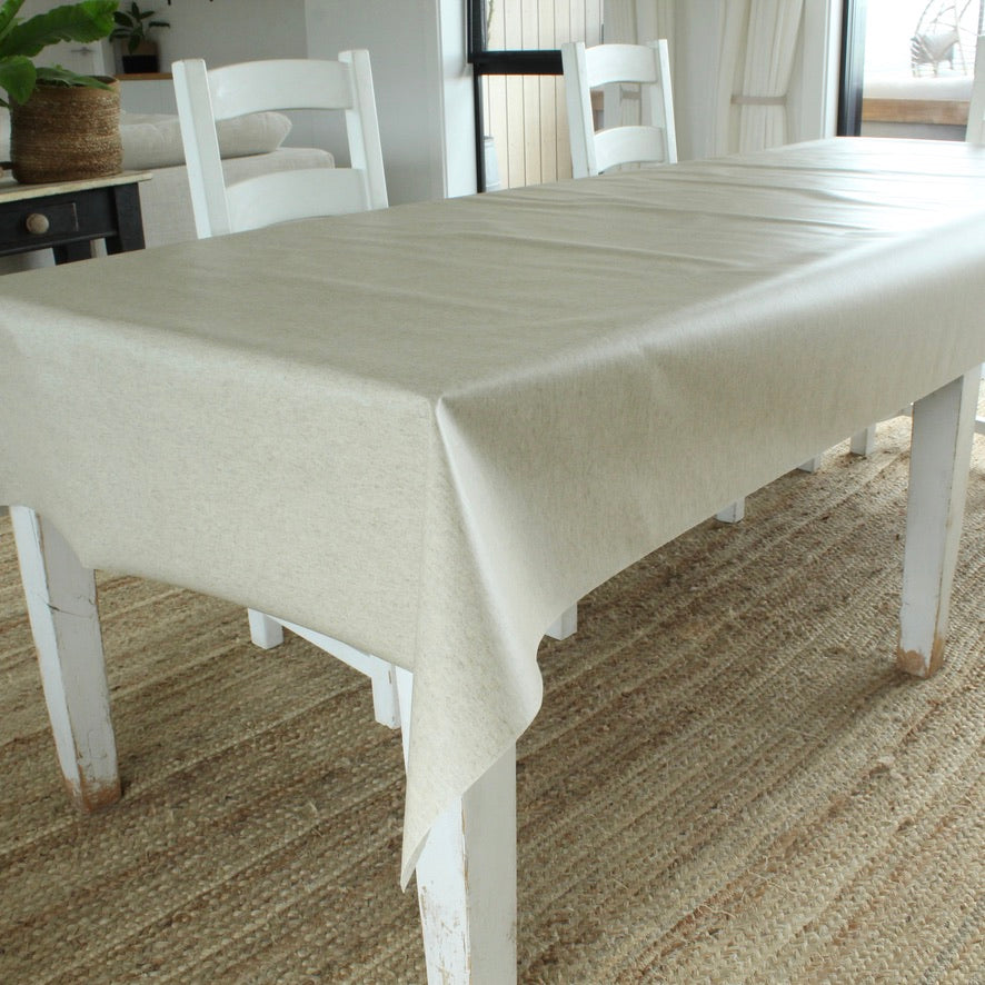 Dining table with a beige tablecloth in a room with chairs and decor.