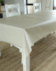 Dining table with a beige tablecloth in a room with chairs and decor.