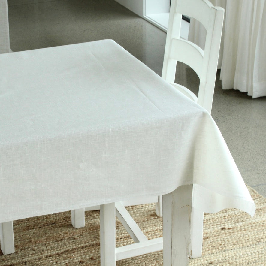White tablecloth on a white table with chairs in a room setting.