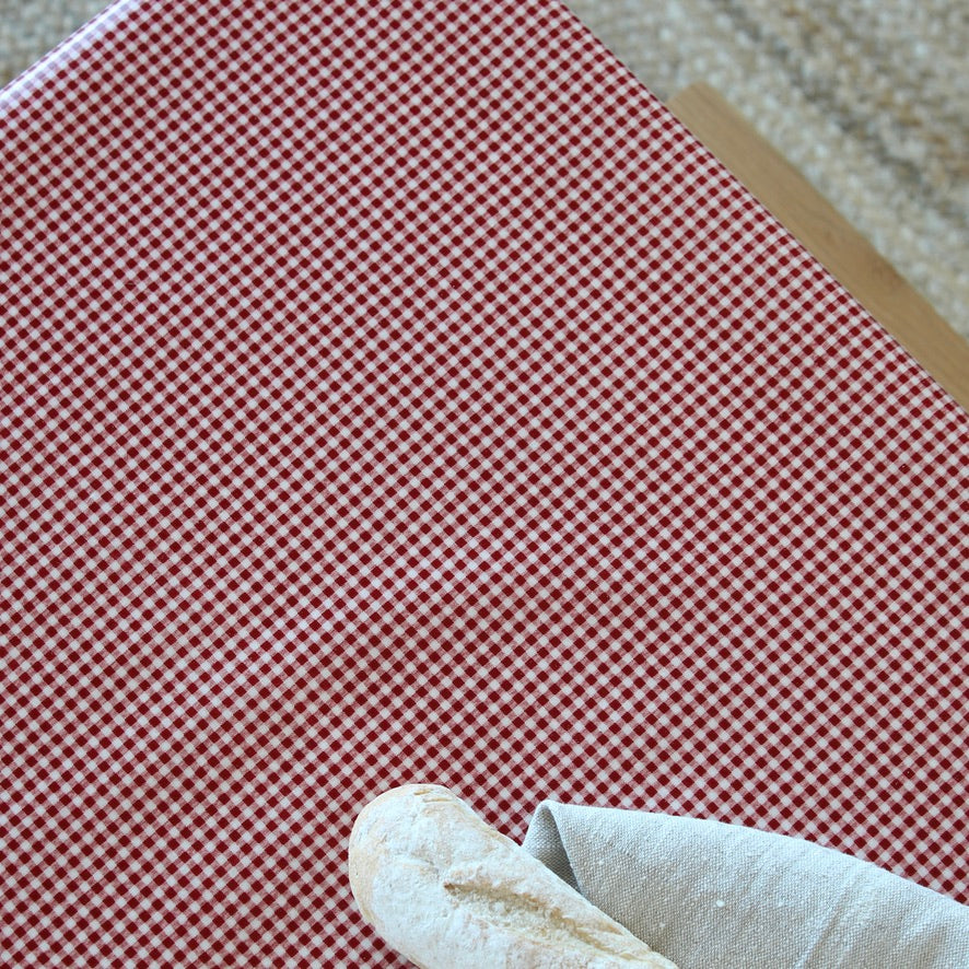 A close-up of a red and white gingham patterned tablecloth, with a white cloth and a small beige object partially visible in the lower corner.