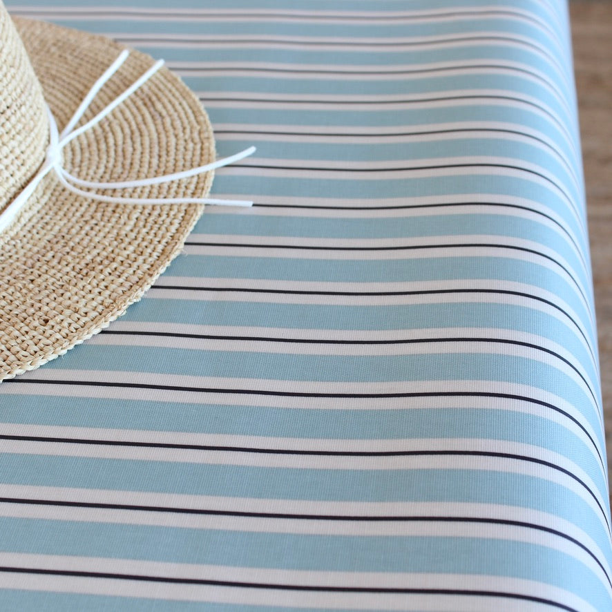 Close-up of a straw hat on a striped oilcloth with blue and white stripes.