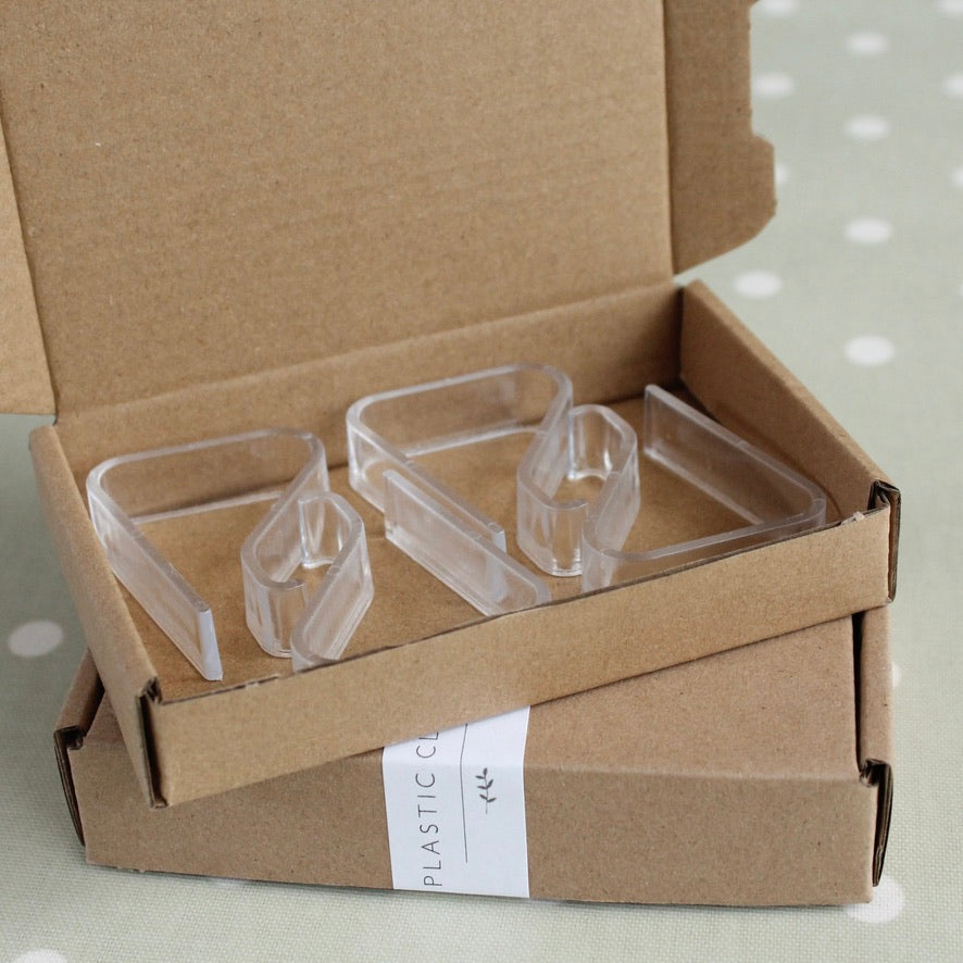Clear plastic tablecloth clips in an open cardboard box on a light background