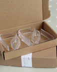 Clear plastic tablecloth clips in an open cardboard box on a light background