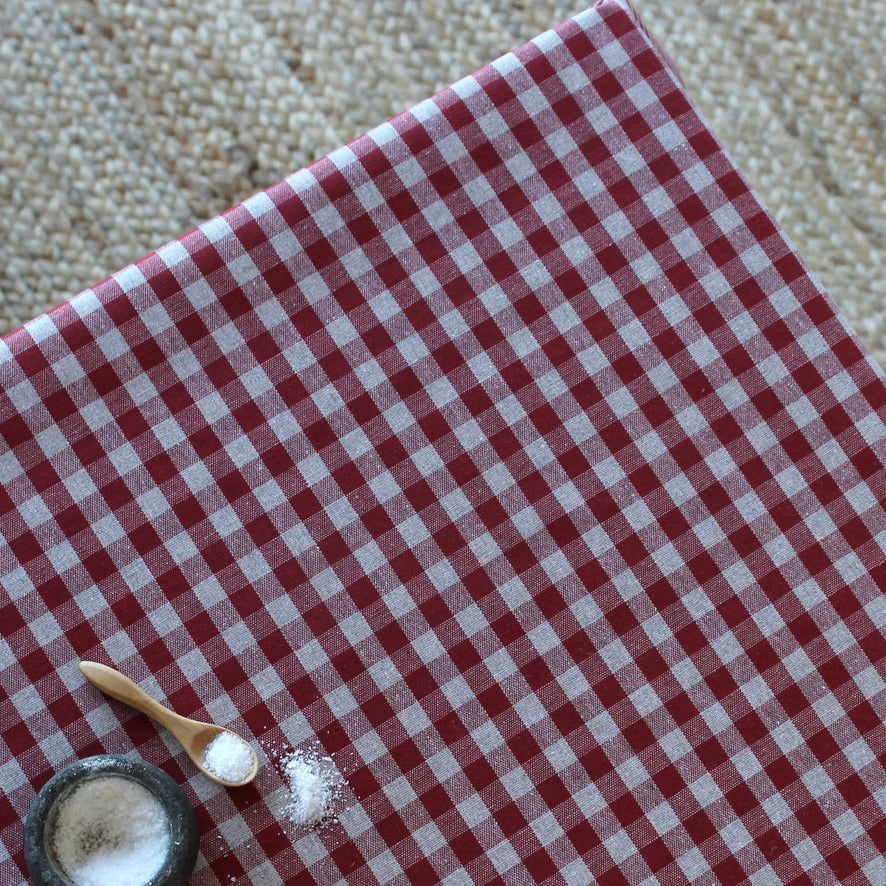 Red and white checkered tablecloth with a wooden spoon and small container on a textured surface
