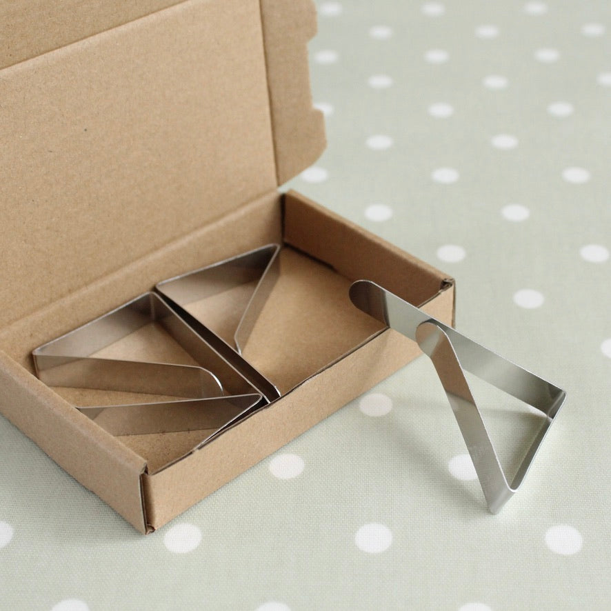 Metal tablecloth clips in an open cardboard box on a polka dot oilcloth