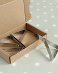 Metal tablecloth clips in an open cardboard box on a polka dot oilcloth