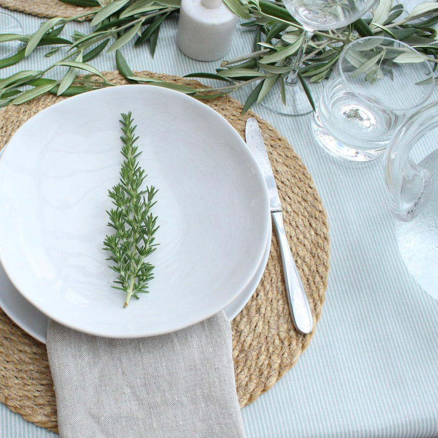 Table setting with white plates, greenery, and cutlery on a green stripe oilcloth