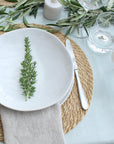 Table setting with white plates, greenery, and cutlery on a green stripe oilcloth