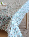 A light sage green tablecloth with a white cherry blossom branch pattern, draped over a wooden table in a softly lit room.
