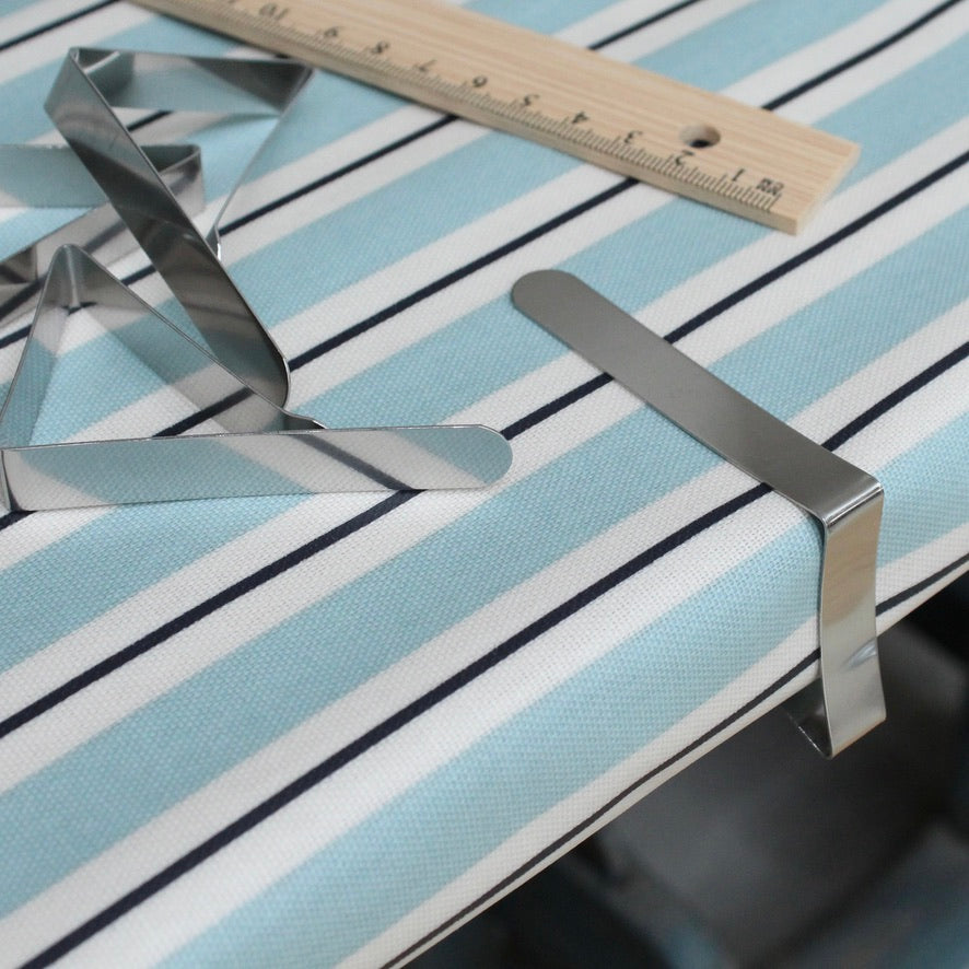 Metallic tablecloth clips on a striped oilcloth background with a ruler for scale.