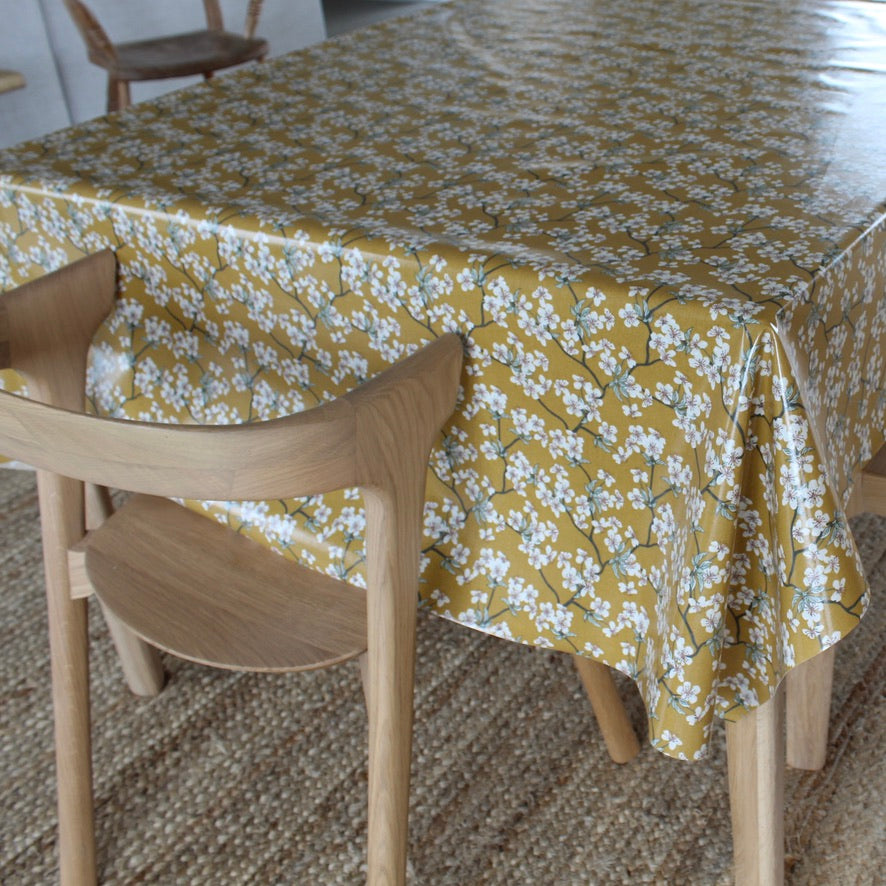 Table with a yellow floral tablecloth and a wooden chair.