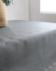 Grey green tablecloth on a table with a woven basket and plant in the background