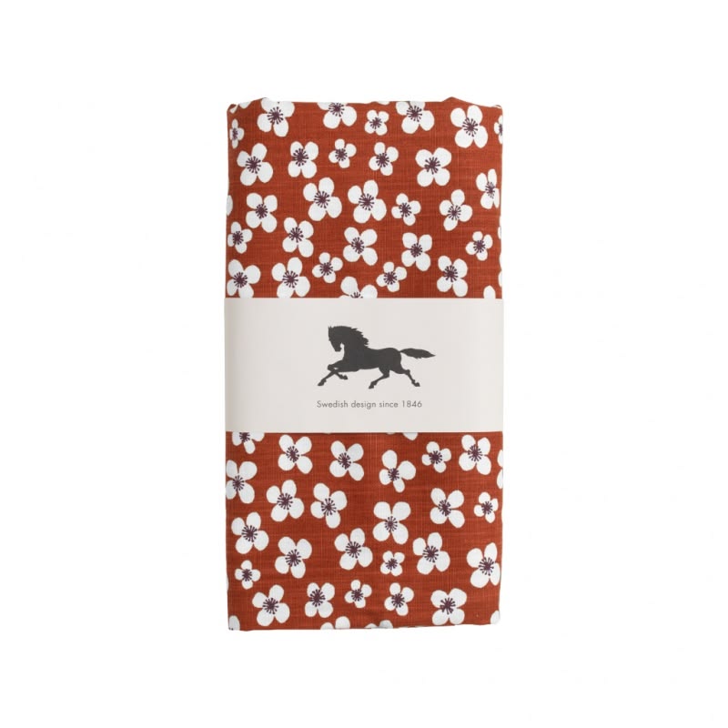 A folded oilcloth featuring a rust-orange background with a white floral pattern. It is wrapped in a white paper band with a black horse logo and the text 'Swedish design since 1846'.