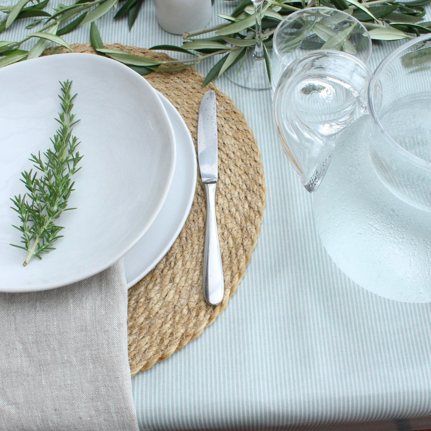Table setting with white plates, silver knife, and glasses on a green stripe tablecloth.