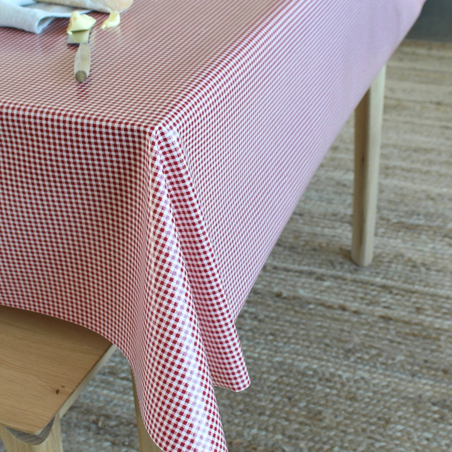 A red and white gingham checkered tablecloth draped over a wooden table in a home setting with a textured rug on the floor.