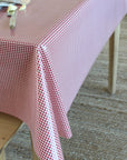 A red and white gingham checkered tablecloth draped over a wooden table in a home setting with a textured rug on the floor.
