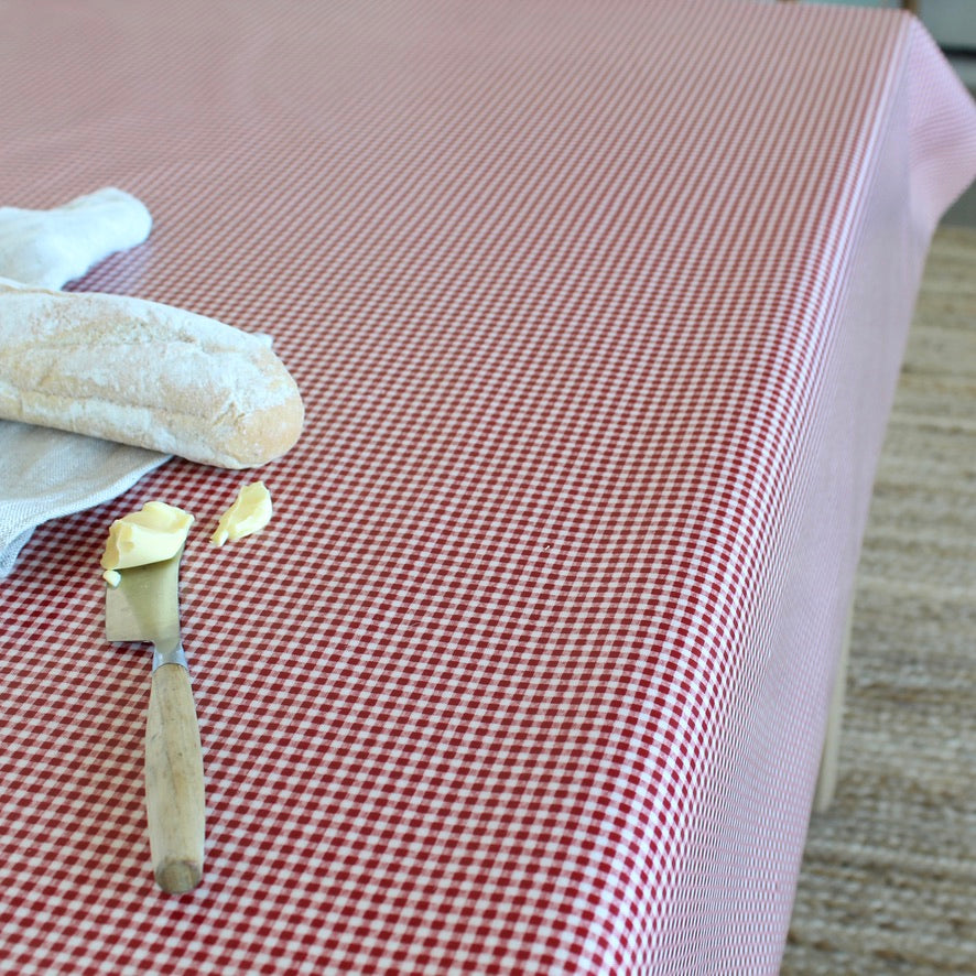 A red and white gingham checkered tablecloth spread across a table, styled with a baguette, butter, and a knife in the foreground.