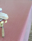 A red and white gingham checkered tablecloth spread across a table, styled with a baguette, butter, and a knife in the foreground.