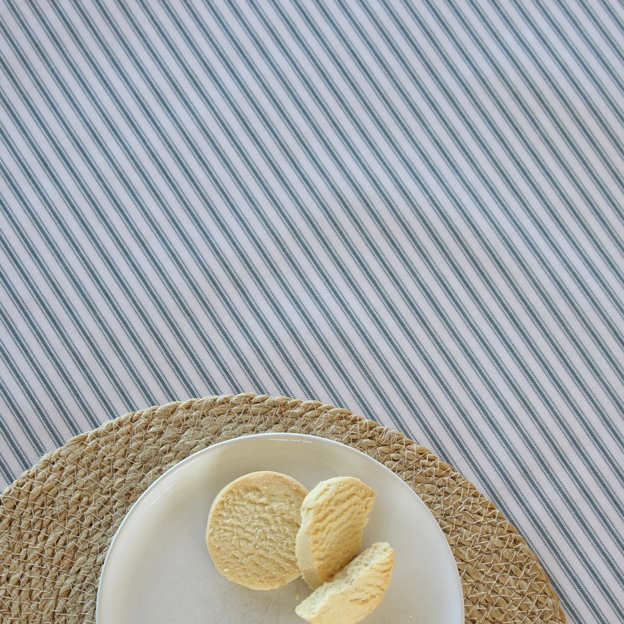 Three cookies on a white plate with a woven placemat on a striped tablecloth.