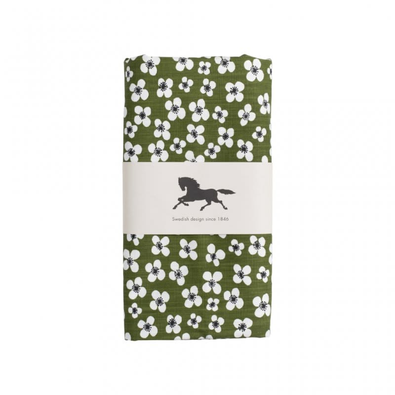 A folded green oilcloth with a white and black floral pattern, wrapped in a white paper band featuring a black horse logo and the text 'Swedish design since 1846'.