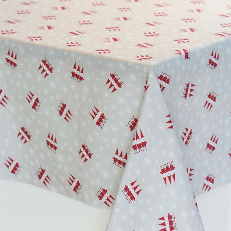 A tablecloth with a festive holiday pattern, featuring red Christmas tree silhouettes and small white snowflakes on a light gray base, draped over the corners of a table.