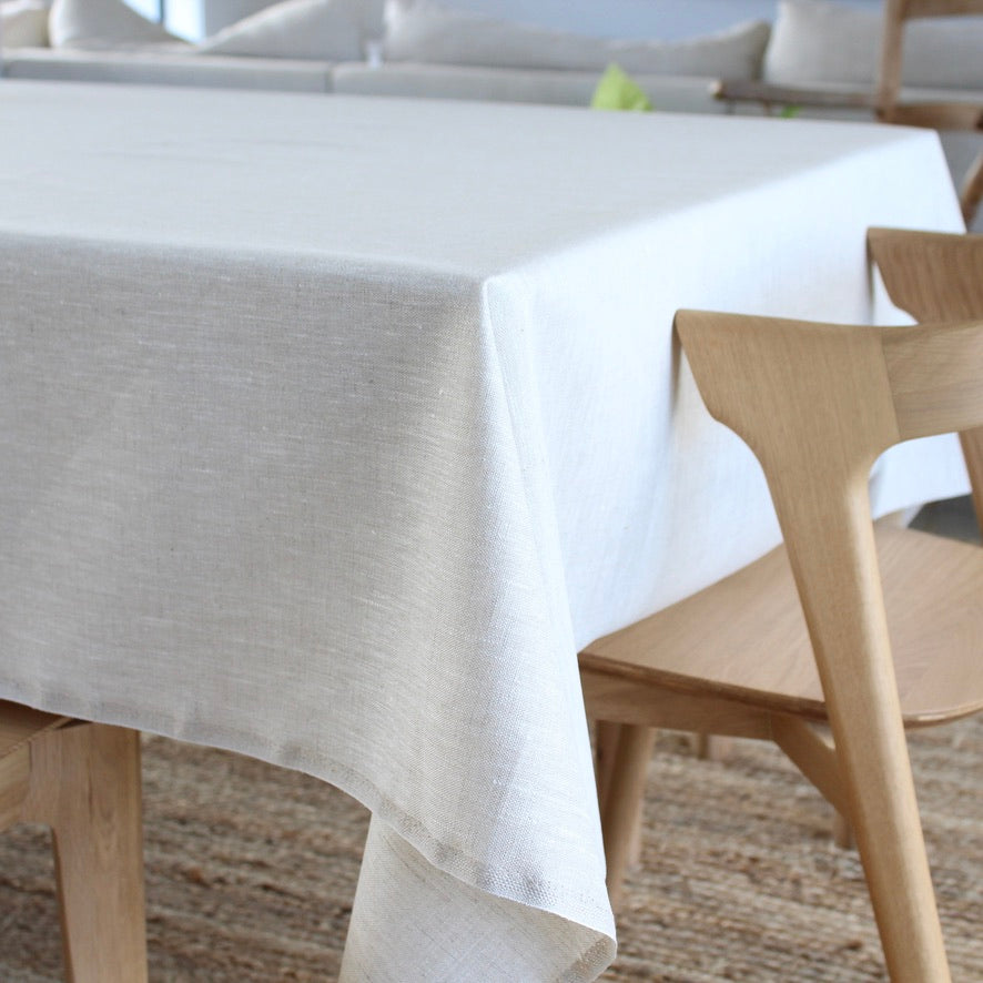 beige tablecloth on a wooden table with chairs in the background