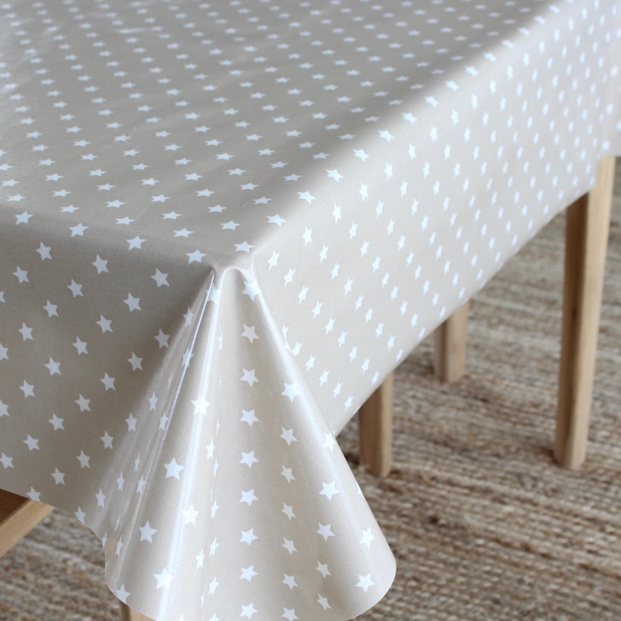 A light beige tablecloth with a white star pattern draped over a table with wooden legs on a woven rug.