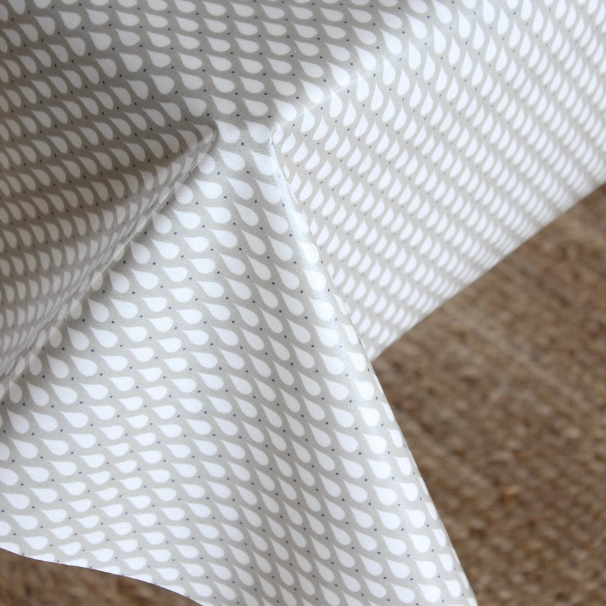 White tablecloth with a repeating gray leaf or teardrop pattern, draped over a table with a textured beige woven surface visible underneath.