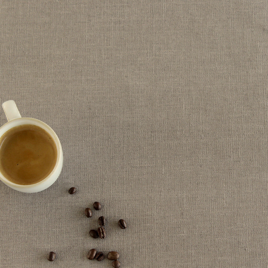 White cup of coffee and scattered coffee beans on a beige linen tablecloth