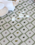 White plush toy on a patterned green and white oilcloth with water droplets