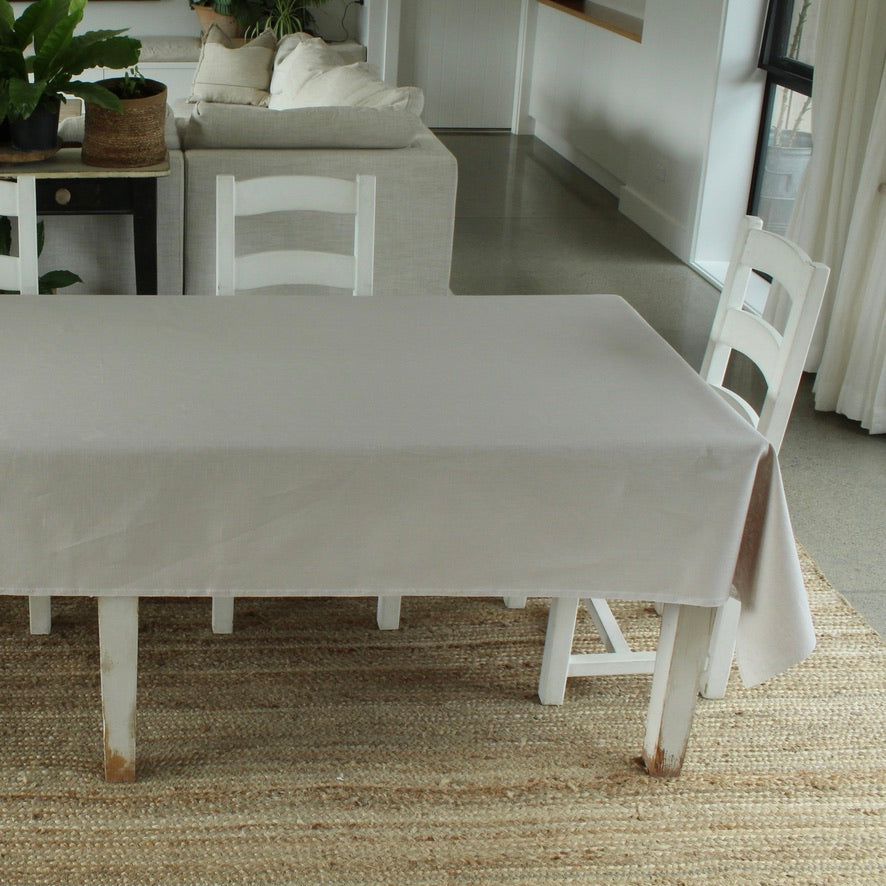 Dining table with a grey linen tablecloth in a room with a rug and chairs.