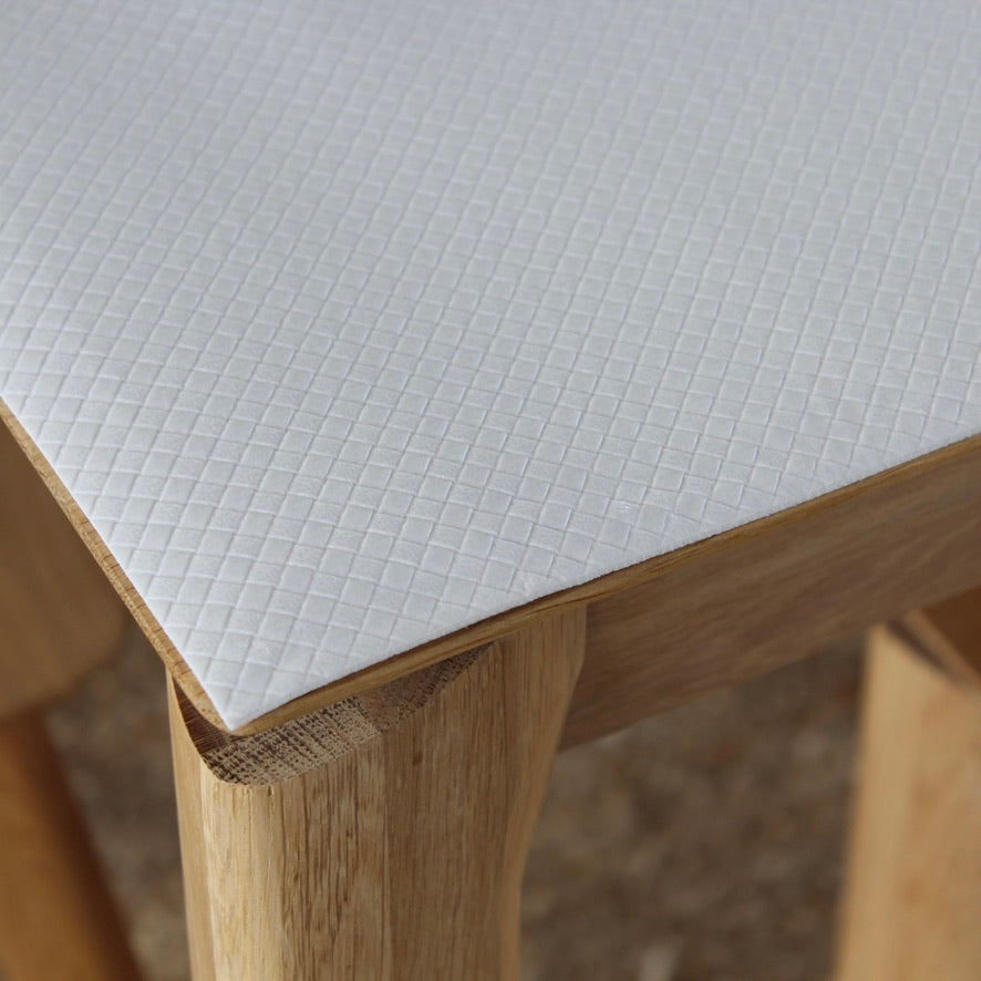 Close-up of a white textured table mat with a subtle grid pattern, shown on a light wood table.