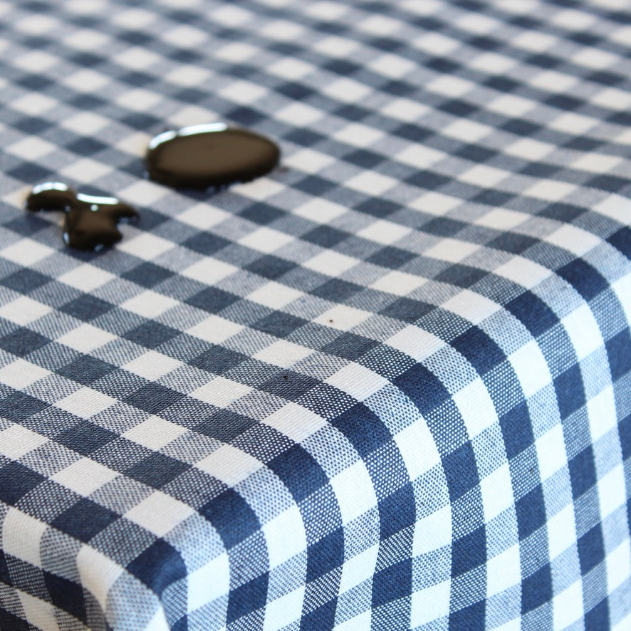 A close-up of a navy blue and white gingham checkered wipe clean tablecloth with balsamic vinegar spilled onto it.