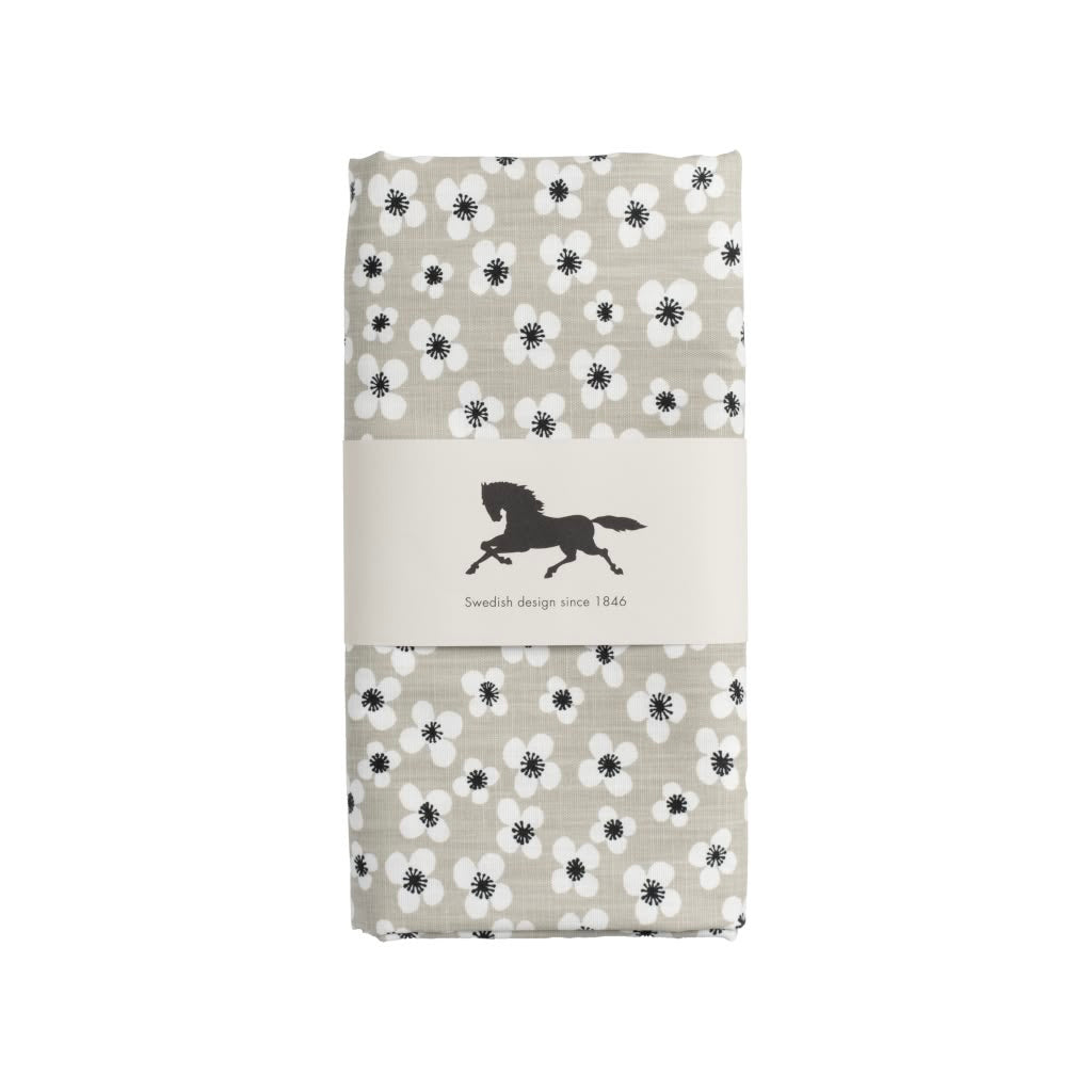 A folded oilcloth featuring a black and white floral pattern on a light beige background, wrapped in a neutral paper band with a black horse logo and the text 'Swedish design since 1849'.