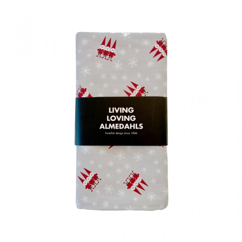 A folded oilcloth featuring a repeating pattern of red christmas gnomes and white snowflakes, wrapped in a black paper band with the text 'LIVING LOVING ALMEDAHLS'.