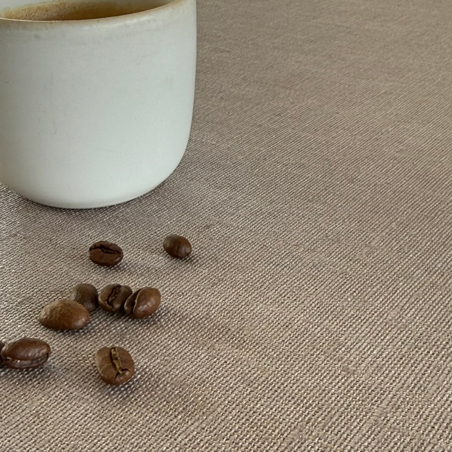 White ceramic cup and coffee beans on a textured beige linen tablecloth