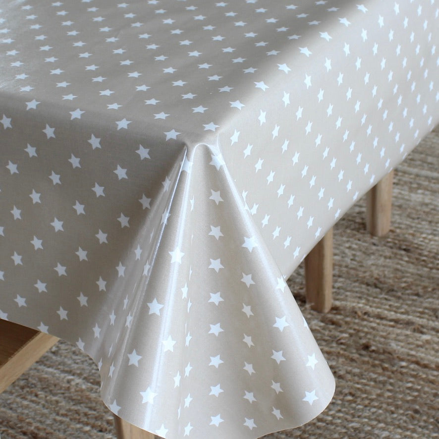 A light beige tablecloth with a white star pattern draped over a table, with wooden table legs and a woven rug visible underneath.