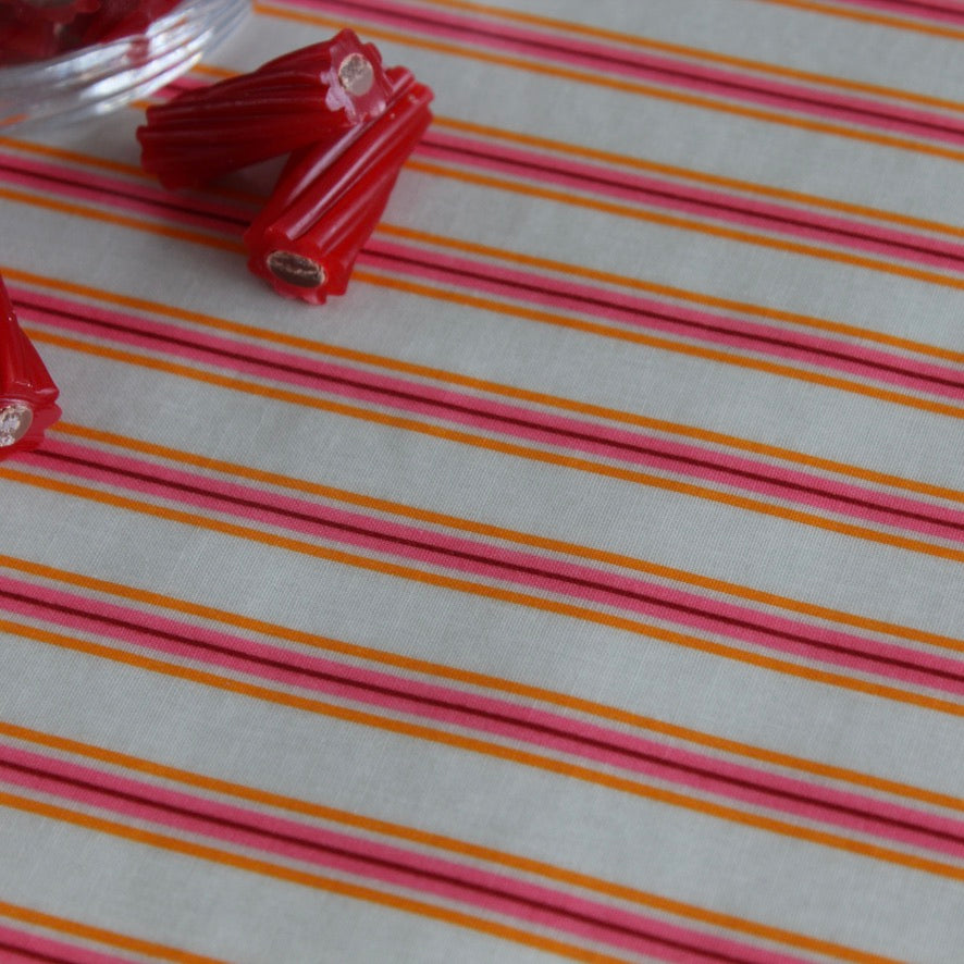 A close-up of a striped oilcloth with alternating pink, orange, and white horizontal lines, with small red cylindrical beads or clips placed near the top left on top of the fabric.