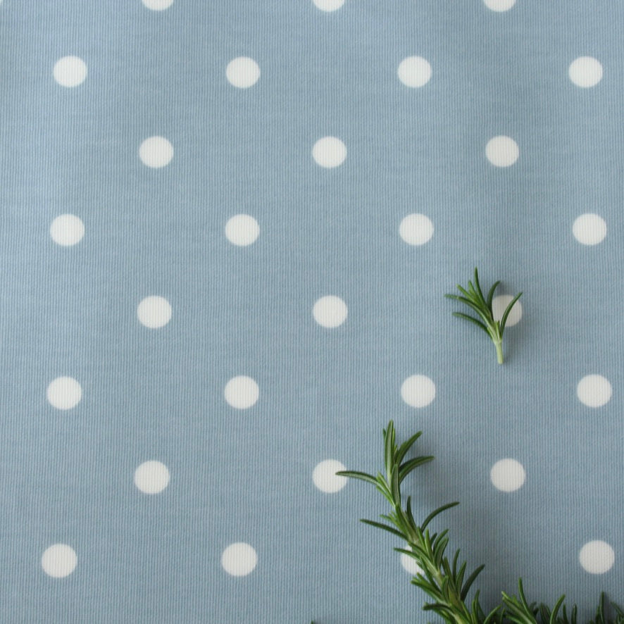 Oilcloth with white polka dots on a blue background with green leaves.