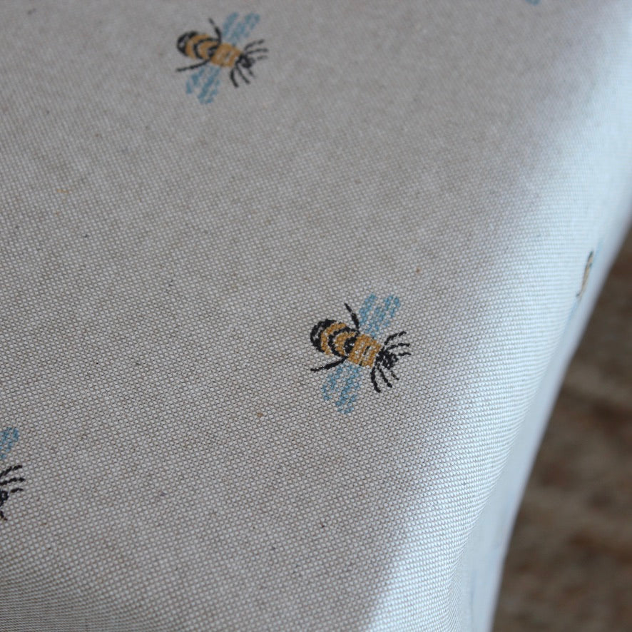 Close-up of tablecloth with embroidered bee designs on a neutral background