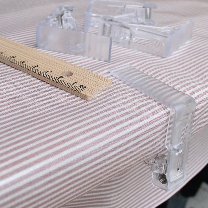 Clear plastic tablecloth clips on a striped oilcloth surface with a wooden ruler for scale.