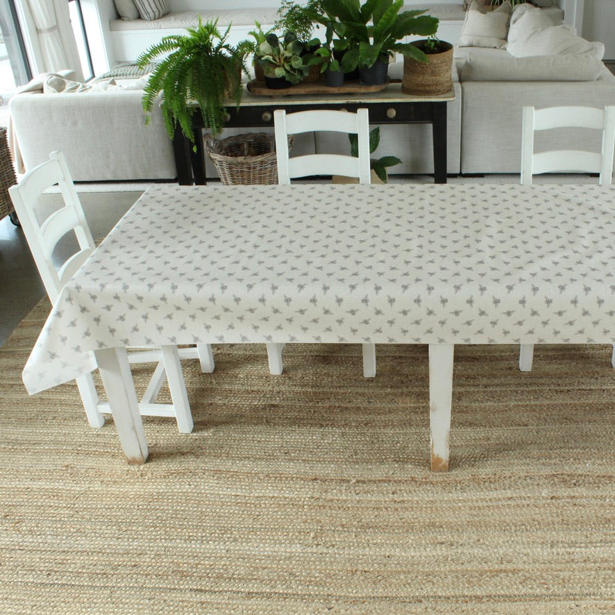 Bee pattern tablecloth in a dining room with a table and chairs on a textured rug, plants in the background